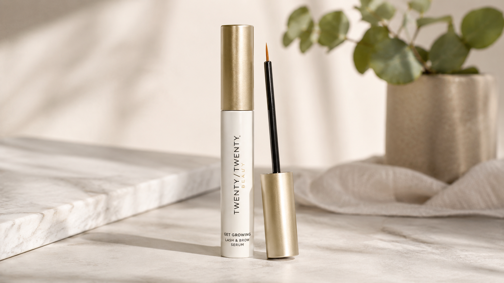 Twenty/Twenty Beauty Get Growing Lash & Brow Serum standing on a marble surface with the applicator wand displayed beside the tube in a soft, minimalist beauty setting for eyelash and eyebrow growth.
