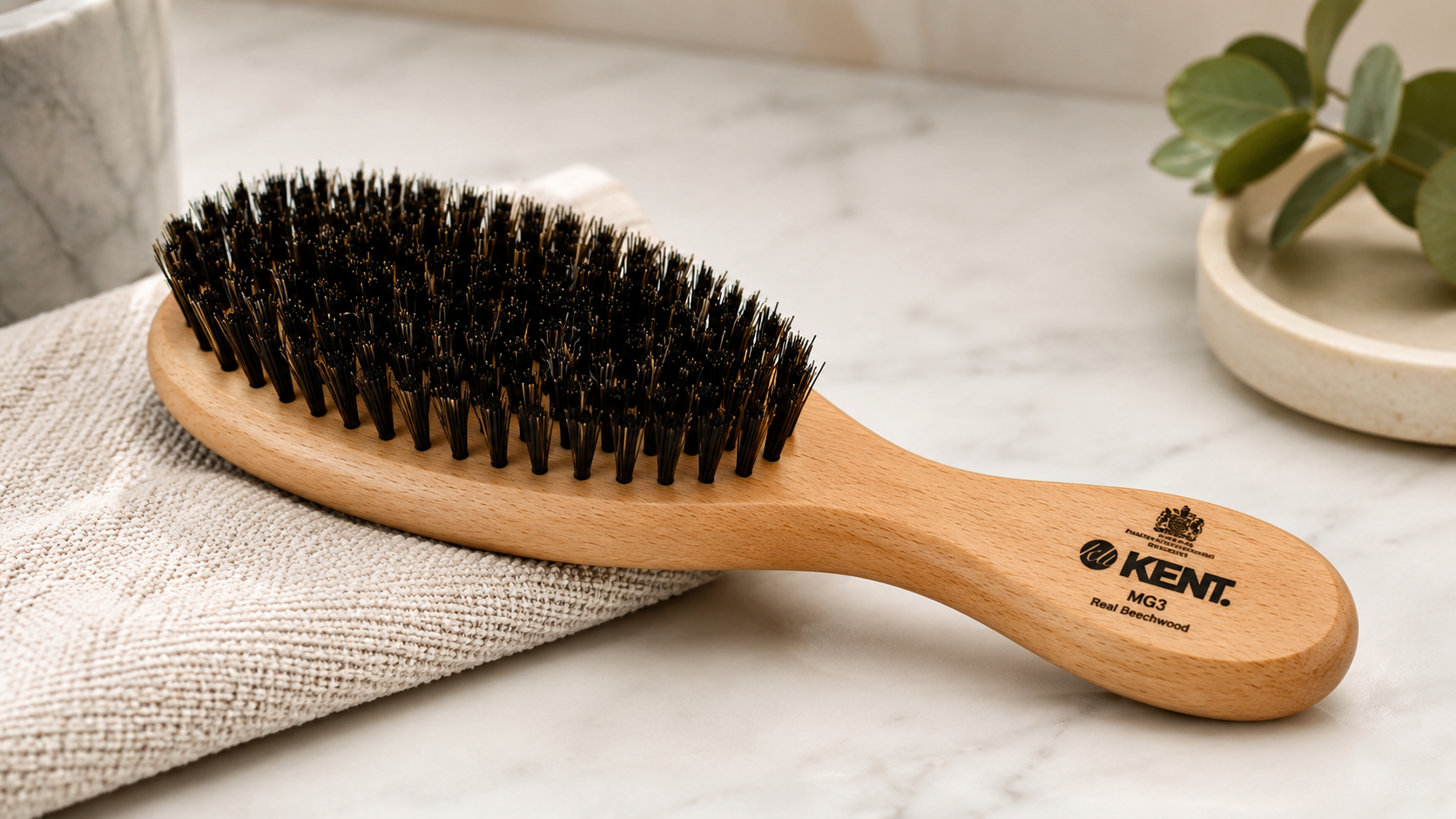 Kent MG3 Beechwood hair brush with natural black bristles resting on a folded towel on a marble countertop in a bright, spa-inspired bathroom setting.