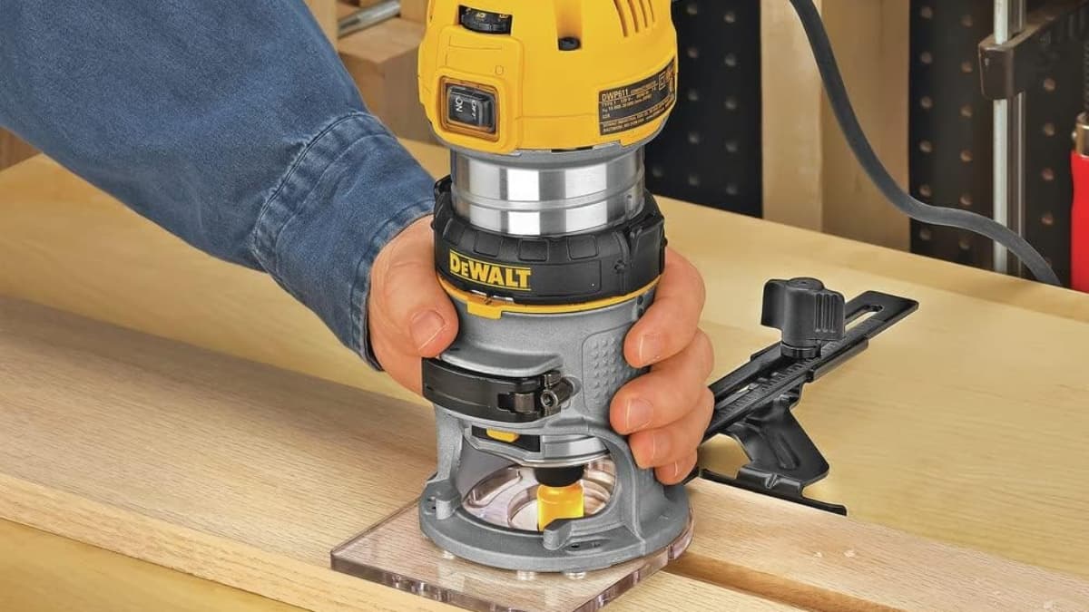 Person using a DEWALT fixed base router to cut wood on a workbench.