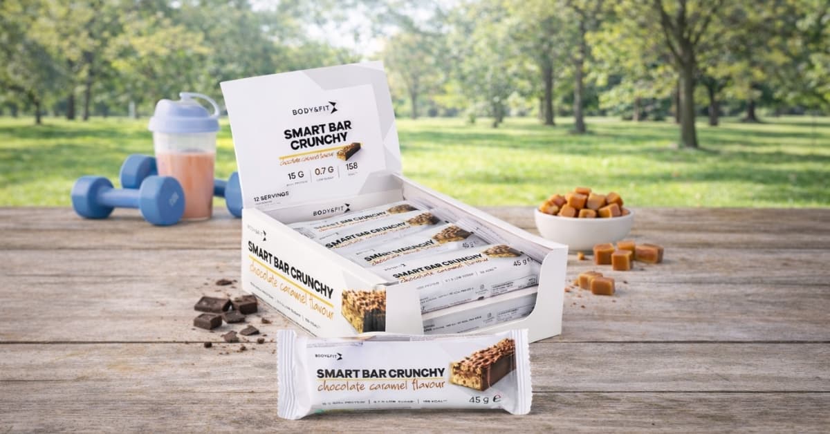 Body & Fit Smart Bar Crunchy chocolate caramel protein bars displayed with gym gear outdoors