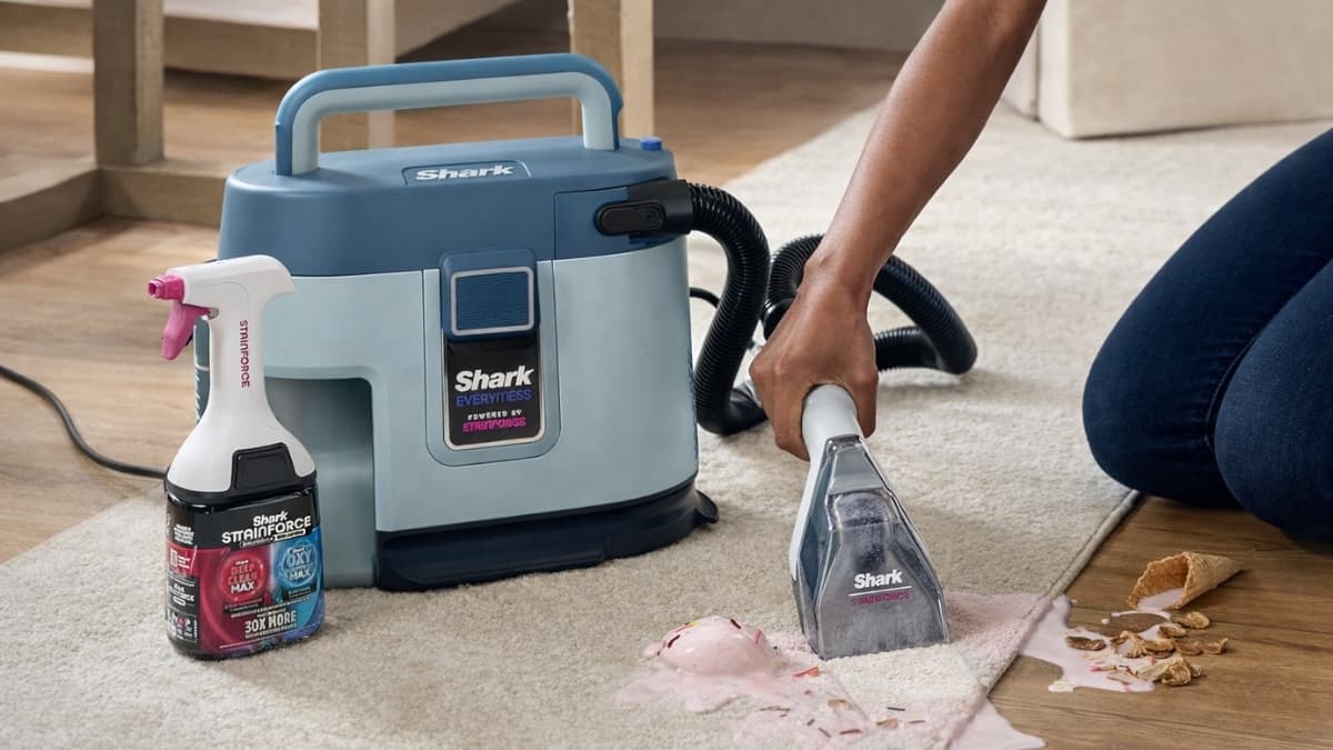 Shark EveryMess Ultra-Powerful 3-in-1 Vacuum cleaning pink spill from carpet next to hardwood floor with StainForce solution bottle visible