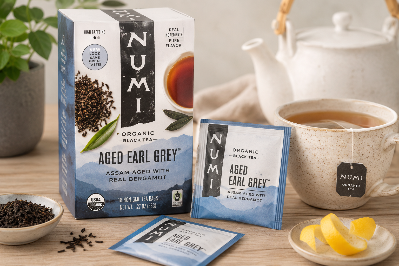Numi Organic Aged Earl Grey Tea box with brewed black tea, bergamot lemon peel, and tea bags on a rustic wooden table in a cozy kitchen setting.