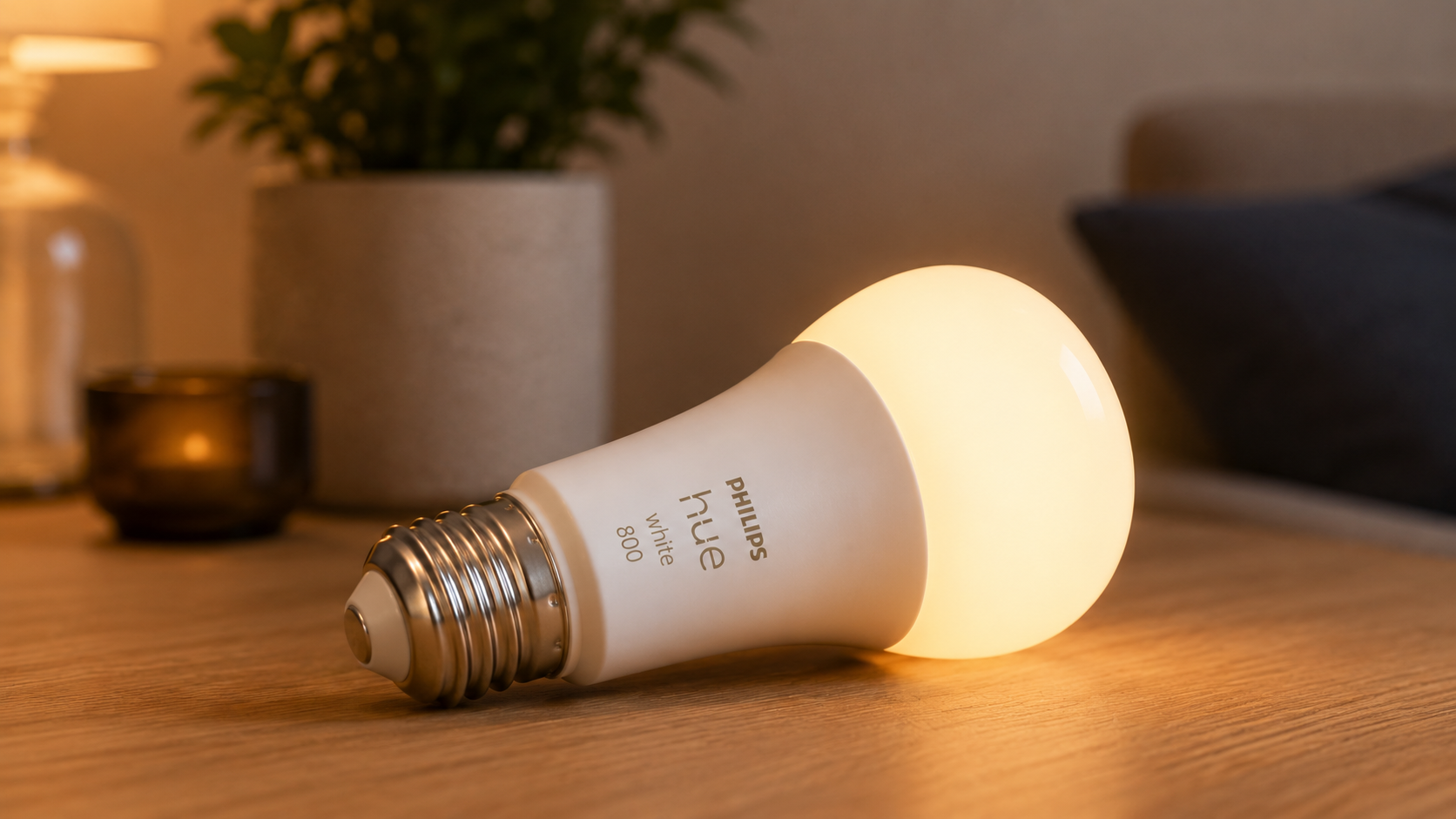 Philips Hue A19 Smart LED bulb lying horizontally on a wooden table, emitting warm white light in a modern smart home setting with soft ambient background lighting.