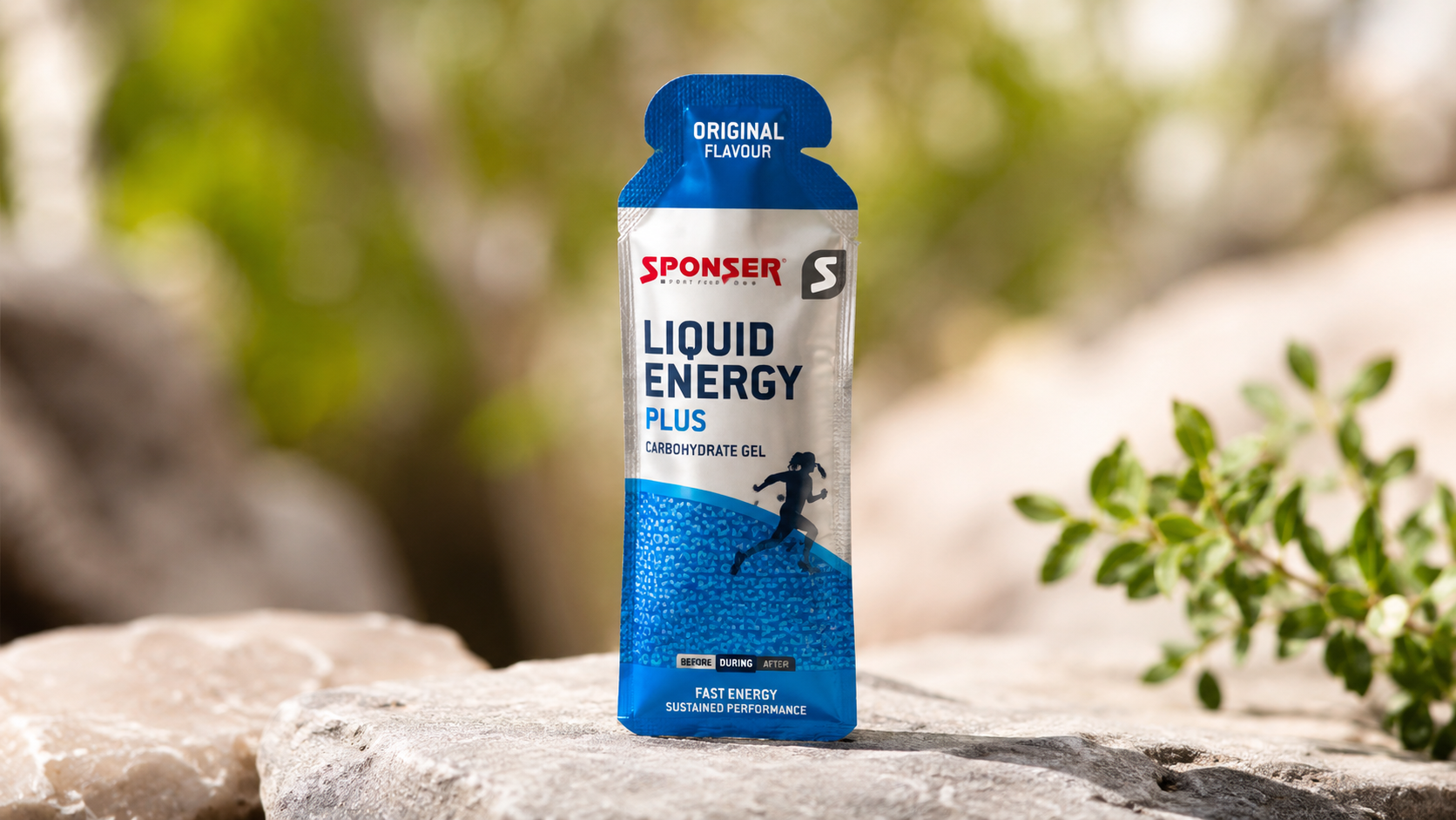 Sponser Liquid Energy Plus Gel carbohydrate energy gel pouch standing on a rock outdoors, designed to provide fast energy and sustained endurance for runners, cyclists, and endurance athletes.